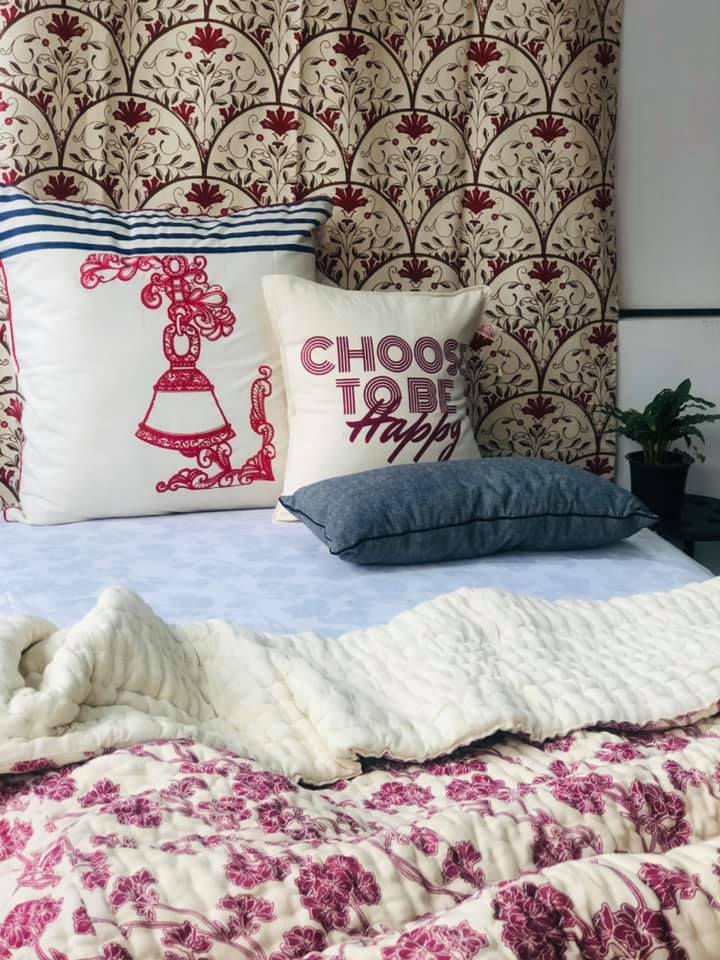 Bedding made by Cotton Mill Nepal featuring floral prints, a pillow with a bell, and a pillow that reads "Choose to be happy"