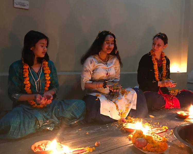 Three girls sit in a row during Mha Puja