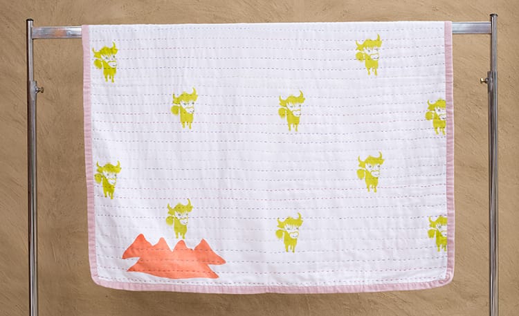 A white baby blanket with pictures of cartoon yaks and mountains by Ramalaya