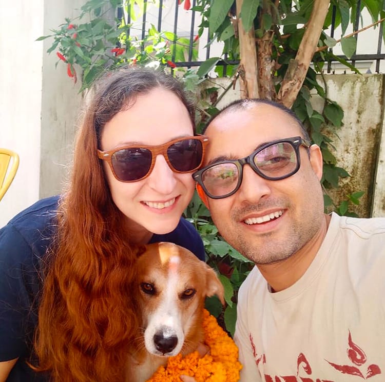 Michelle Della Giovanna from Full Time Explorer and her husband hug their rescue dog while he wears a marigold garland on Kukur Tihar