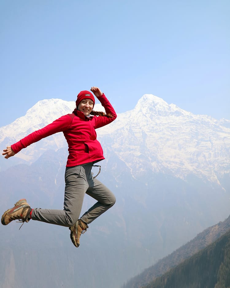 Michelle Della Giovanna from Full Time Explorer jumps in the air in front of the Annapurna range after completing the Mardi Himal Trek Itinerary