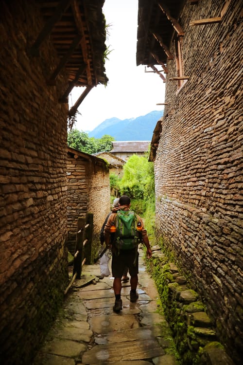 Suraj walks between two old stone buildings in Ghandruk