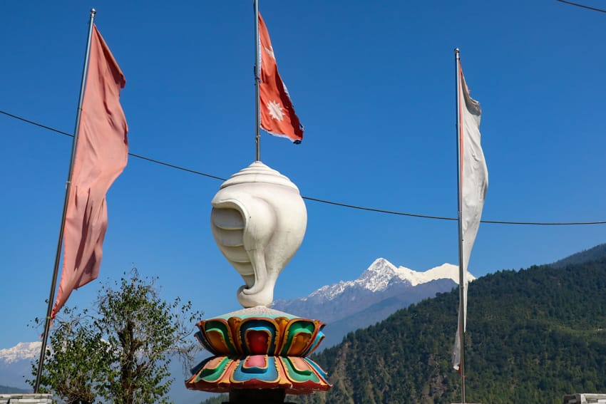 A statue of a conch with the Nepali flag coming out of it and the Langtang mountains in the background taken in Syabrubesi