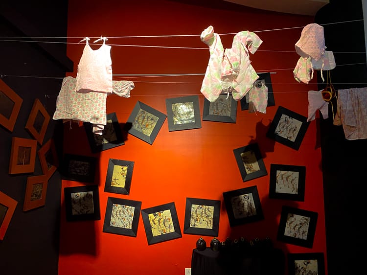 An exhibit inside MONA (Museum of Nepali Art) where traditional Nepali kids clothing are hung from laundry lines in front of black and white drawings - Places To Visit in Kathmandu