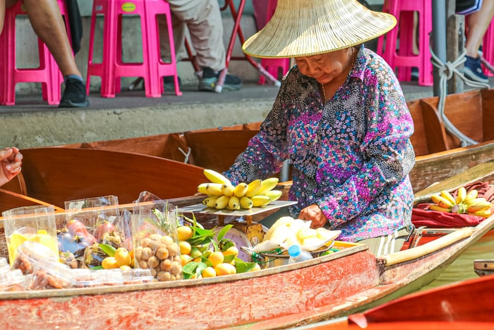 A woman sells fruits out of a boat at Damnoen Saduak Floating Market