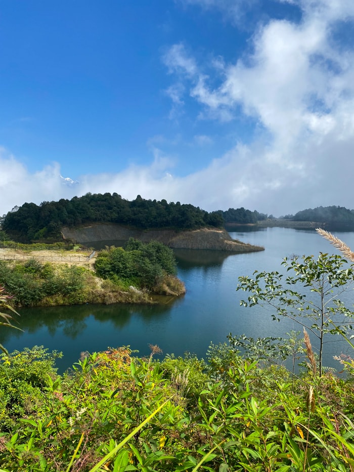 Dhap Dam from the viewpoint with mountains peaking through the clouds in the distance